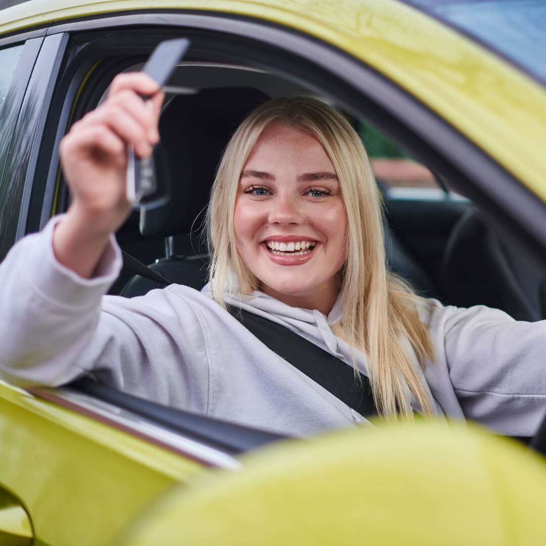 Smiling young woman sitting in a yellow car, holding up her keys after securing an easy bad credit car loan in Australia.