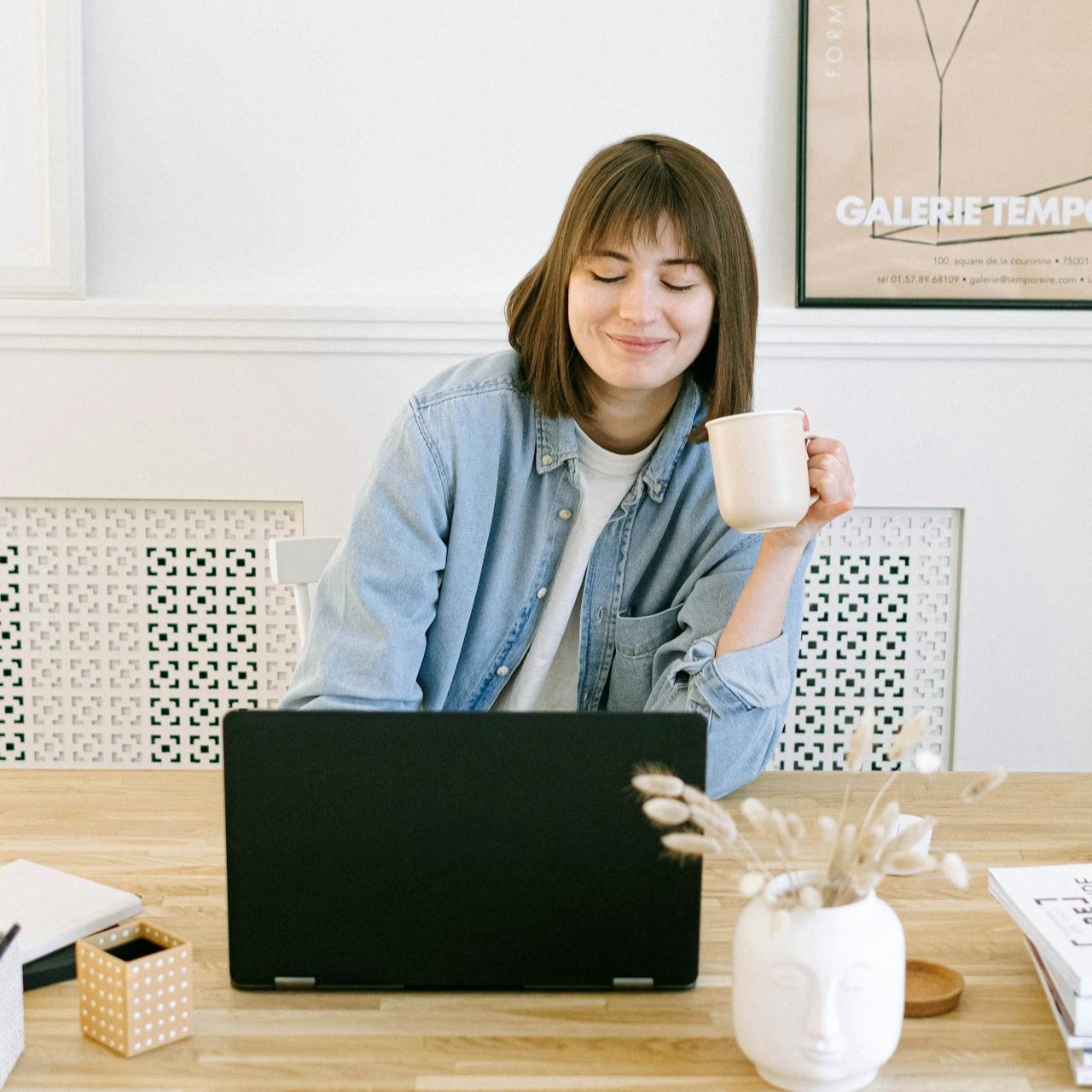 A relaxed woman sitting at a desk with a laptop and a coffee cup, smiling