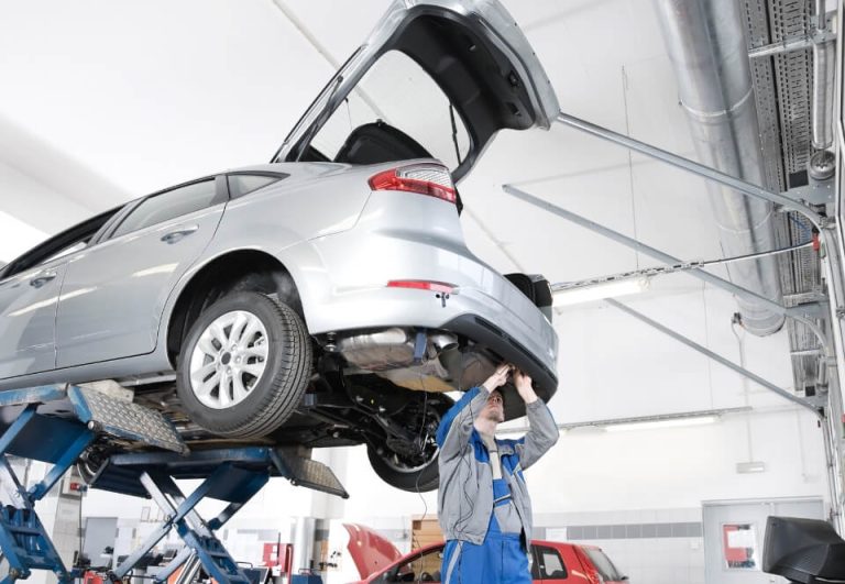 Mechanic inspecting a used car on a hoist in a workshop — part of a pre-purchase vehicle inspection.