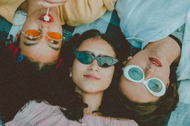 Three people lying on the ground outdoors wearing sunglasses, viewed from above