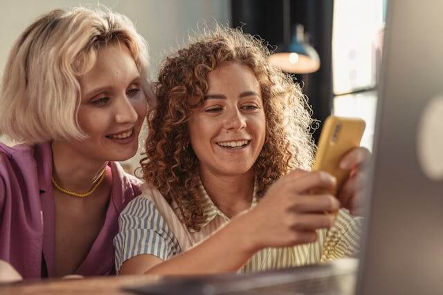 Two women reviewing information on a phone and feeling confident about their loan options.