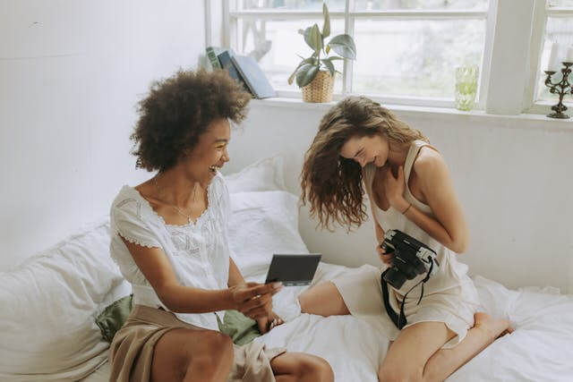 Two people sitting on a bed, looking at a picture they just took on a polaroid camera in a calm, supportive home setting.