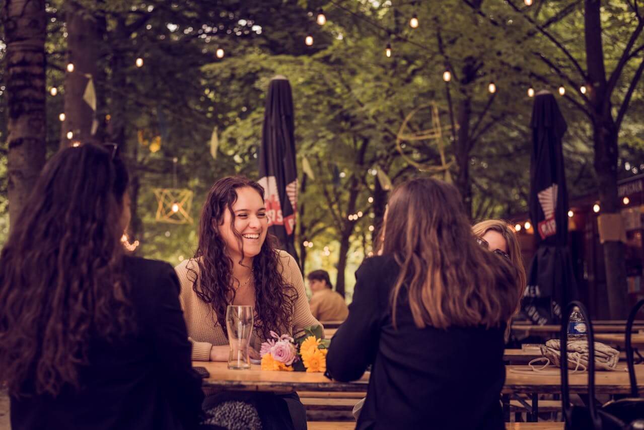 A small group of people sitting at an outdoor table, talking together in a relaxed setting.