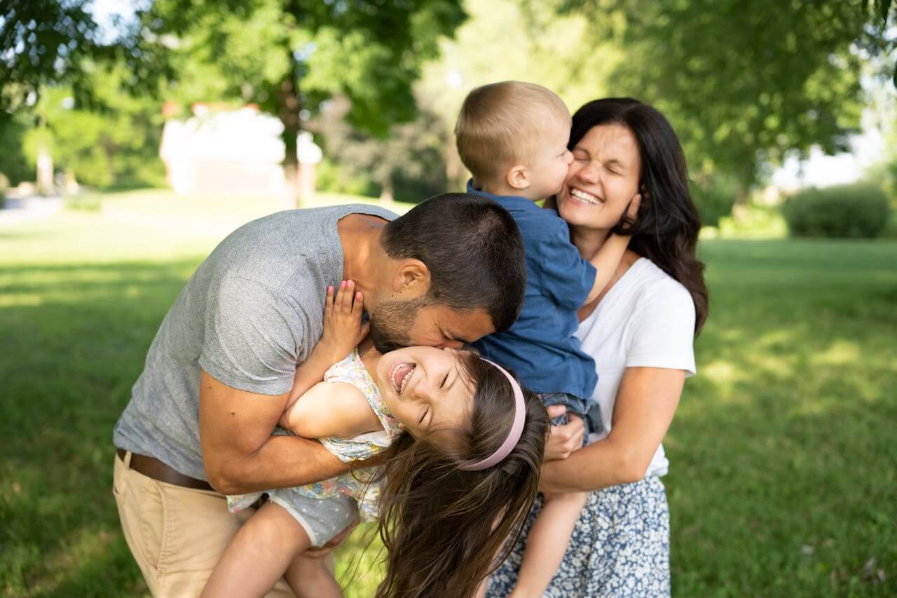 A happy family of four laughs as their photo is taken in a greet outdoors setting.
